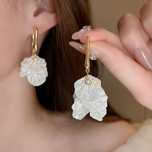 Elegant gold earrings with white acrylic flower petals worn by model in a soft setting