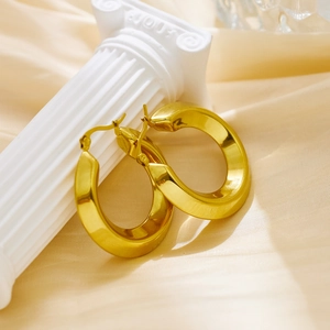Polished gold-tone C-shaped tube earrings on a white marble pillar background