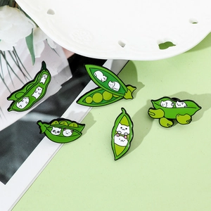 Set of five cute green enamel cat pea pod brooches arranged on textured paper and ceramic decor