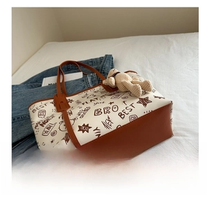 Detail view of the contrasting brown leather base and graffiti prints on the cream tote bag