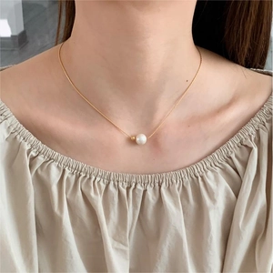 Close-up of a minimalist single pearl necklace with fine gold chain on a female model