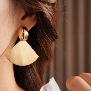 Detailed view of brushed gold fan earrings with oval studs on model for modern style