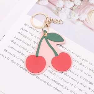 Detail of pink PU leather cherry keychain with golden ring and lobster clasp over a book