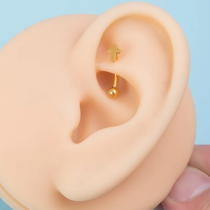 Macro shot of gold cross-shaped piercing jewelry on a realistic ear model for display