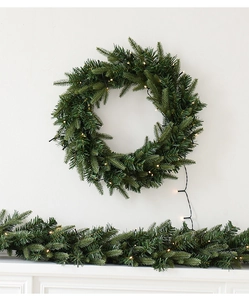 Détail de la couronne de Noël en PE vert et guirlande avec LED chaudes sur mur blanc