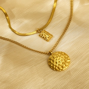 Close-up of golden layered necklaces with honeycomb round and square pendants on satin