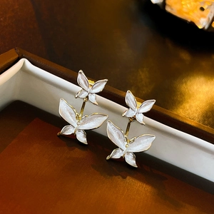 Detailed macro view of gold-trimmed double butterfly stud earrings on a brown jewelry box