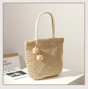 Close-up of handmade beige straw tote bag featuring decorative plush pom-pom charms