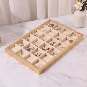 Detail of 24-compartment beige velvet jewelry tray with a gold metal frame on marble