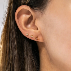 Close-up of a gold starfish stud earring set with red gemstones on a model's ear