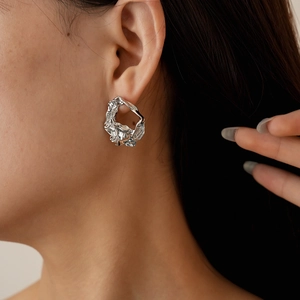 Detailed view of silver irregular metallic earrings with textured fold design on model
