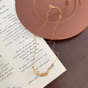 Close-up of golden crescent moon pendant necklace resting on a ceramic dish with textured details