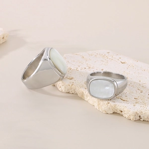Silver stainless steel band ring with white shell inlay set on a beige stone pedestal