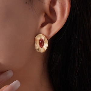 Vue rapprochée d'une boucle d'oreille ovale dorée avec gemme rouge sur l'oreille du mannequin