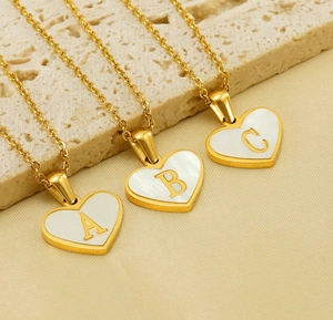 Close-up of gold heart-shaped necklaces with white shell inlay and letter A B C details