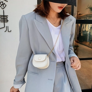 Mini sac selle blanc avec chaîne en métal porté sur un costume bleu clair chic