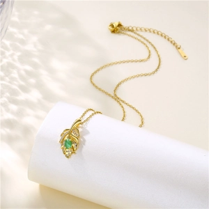 Elegant gold leaf necklace with green oval stone and zircon accents on white podium