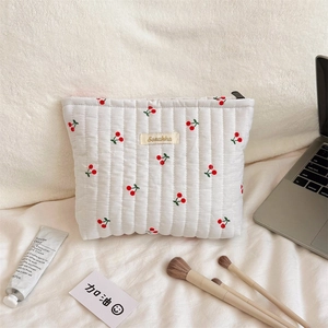 Close-up of white quilted cherry print cosmetic bag with zipper and logo tag