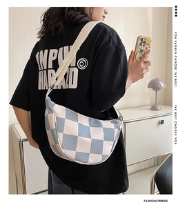 Detail of blue checkerboard knit crescent bag with adjustable cream shoulder strap