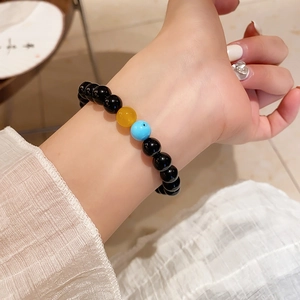 Close-up of black beaded bracelet featuring yellow and blue accent stones on a wrist