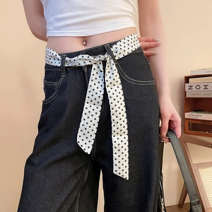 Dettaglio di jeans scuri a vita alta con una sciarpa di seta a pois bianchi e neri in vita
