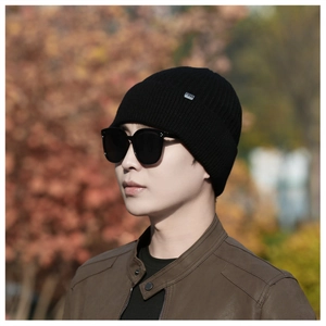 Close-up of black winter knitted beanie with a metal logo tag worn by a male model outdoors