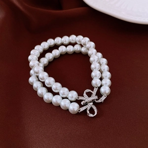 Détail d'un bracelet double rang de perles blanches avec fermoir nœud argenté scintillant