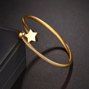 Bracelet jonc doré en acier titane torsadé avec breloque étoile et boule sur fond noir