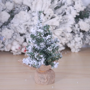 Miniature snow-flocked Christmas tree with green needles and burlap base on wood