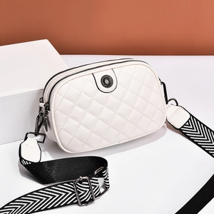 Quilted white crossbody bag with wide herringbone strap and metal flower detail