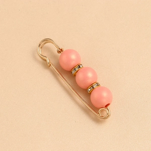 Detail showing a pink bead safety pin brooch with golden rhinestone spacers on a beige surface