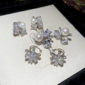Detail of silver earrings with white pearls and zircon stones on a cream textured card