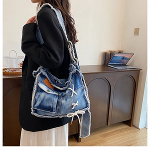 Detail of washed denim shoulder bag with fringe edges and lace-up design on model