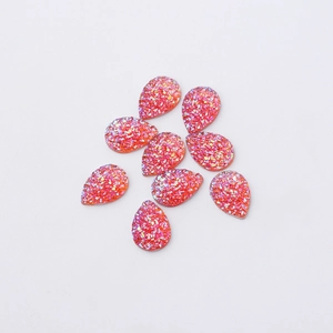 Macro detail of tear-drop shaped resin charms with sparkling orange-pink glitter texture
