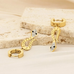 Detailed close-up of golden snake earrings with rhinestones on beige silk and stone