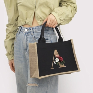 Detail of black canvas tote bag with jute trim and floral letter A print being carried
