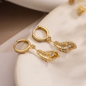 Elegant gold-plated feather drop earrings with sparkling zircon crystals on ceramic plate