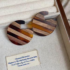 Macro detail of retro C-shaped wood and resin earrings in a premium jewelry display box