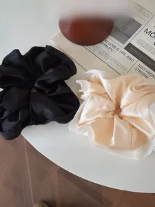 Macro view of luxurious satin oversized scrunchies in black and beige on a white desk