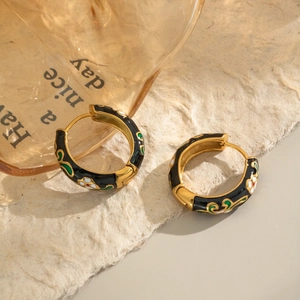 Golden hoop earrings with black enamel and floral pattern on a textured background