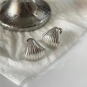 Macro shot of silver shell earrings with radial textures on elegant white silk background
