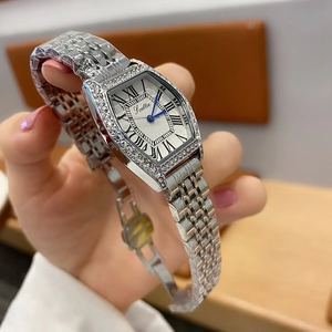 Close-up of silver tonneau watch with diamond bezel and metal chain strap on wrist