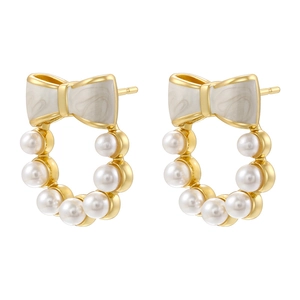 Detailed view of golden bow earrings featuring white enamel and tiny pearls in a wreath