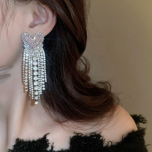 Detail view of heart-shaped silver earrings with sparkling rhinestone tassels worn by a model