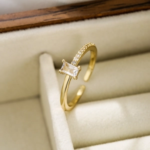 Macro detail of gold-plated geometric ring with rectangular zircon on beige velvet