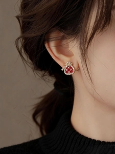 Close-up of elegant red lucky bag earrings with zircon crystals on a female model's ear