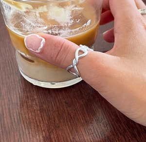 Detailed view of a 925 sterling silver braided ring worn while holding an iced coffee cup
