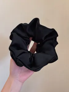Detail of a ruffled black satin scrunchie with subtle luster and pleated texture
