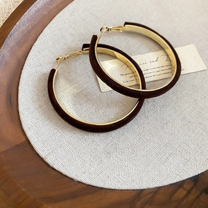 Detail of dark brown velvet hoop earrings on a wooden tray with soft natural lighting