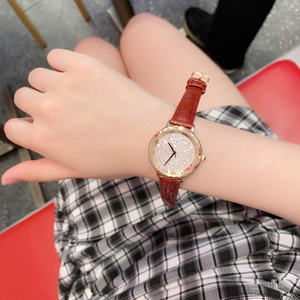Close-up of rose gold watch with crystal dial and reddish brown leather strap on wrist